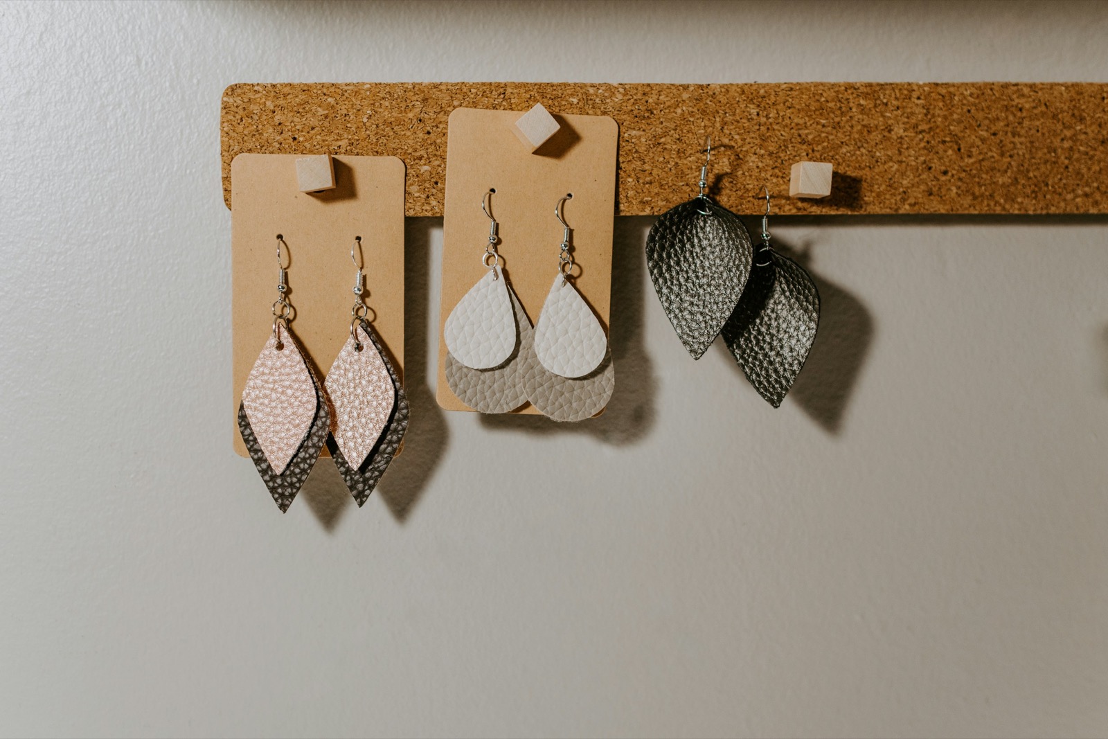 three pairs of hook earrings made from leather hanging on a cork strip in a craft workshop