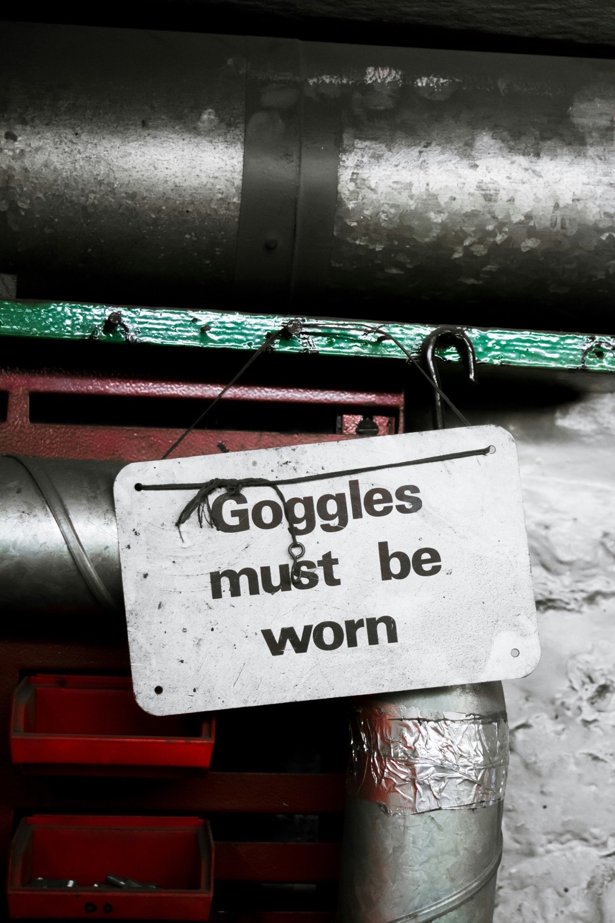 a sign reading goggle must be worn hanging on a nail in an industrial workshop